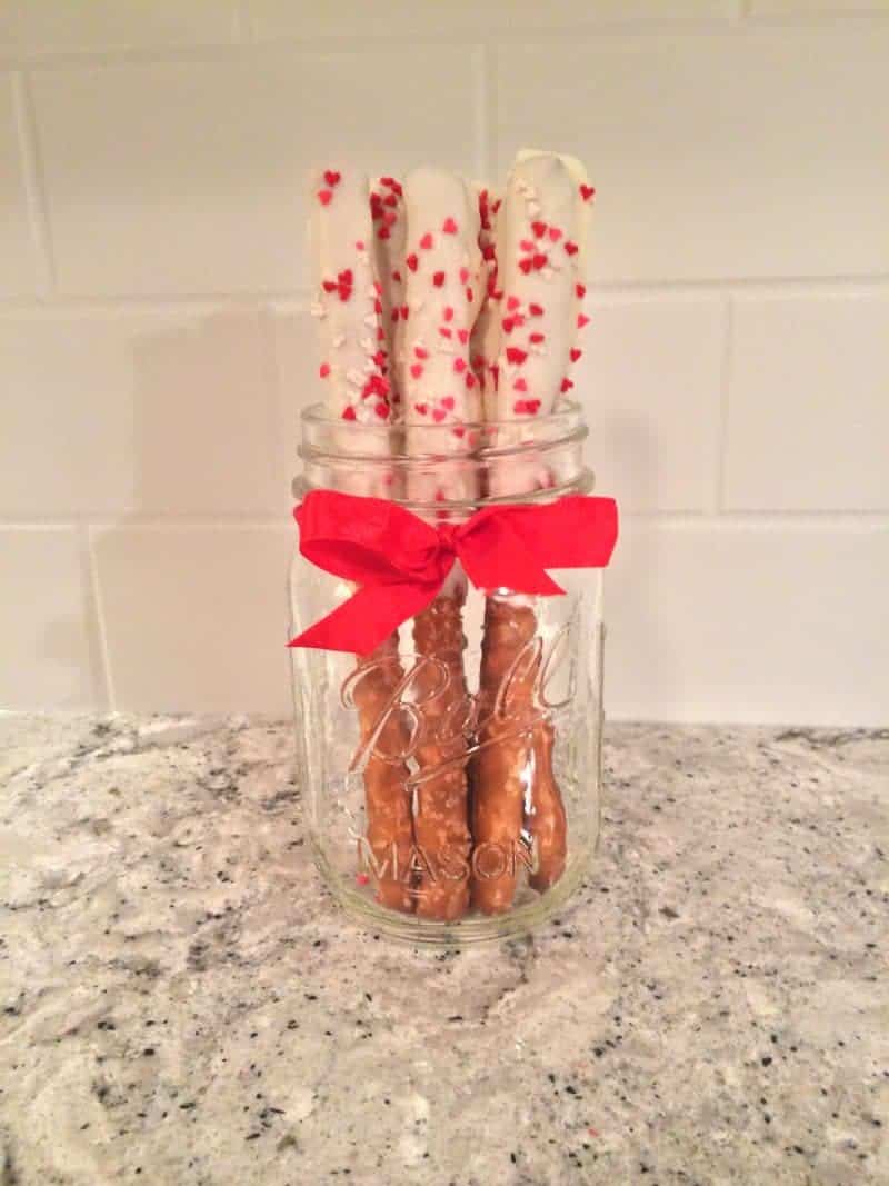 White chocolate dipped Valentine's Day pretzel rods with heart sprinkles.