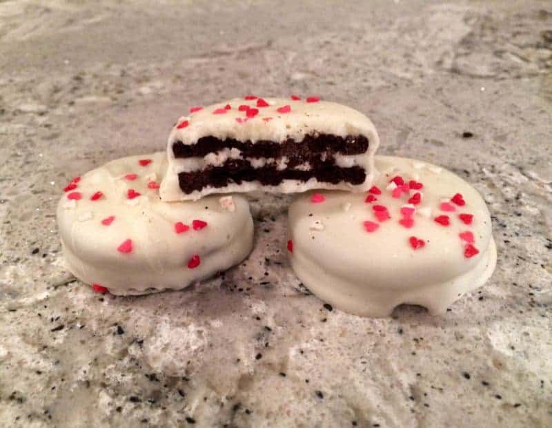 White Chocolate Covered Valentine's Day Oreos with heart sprinkles. Once cookie is bit in half to show oreo inside.