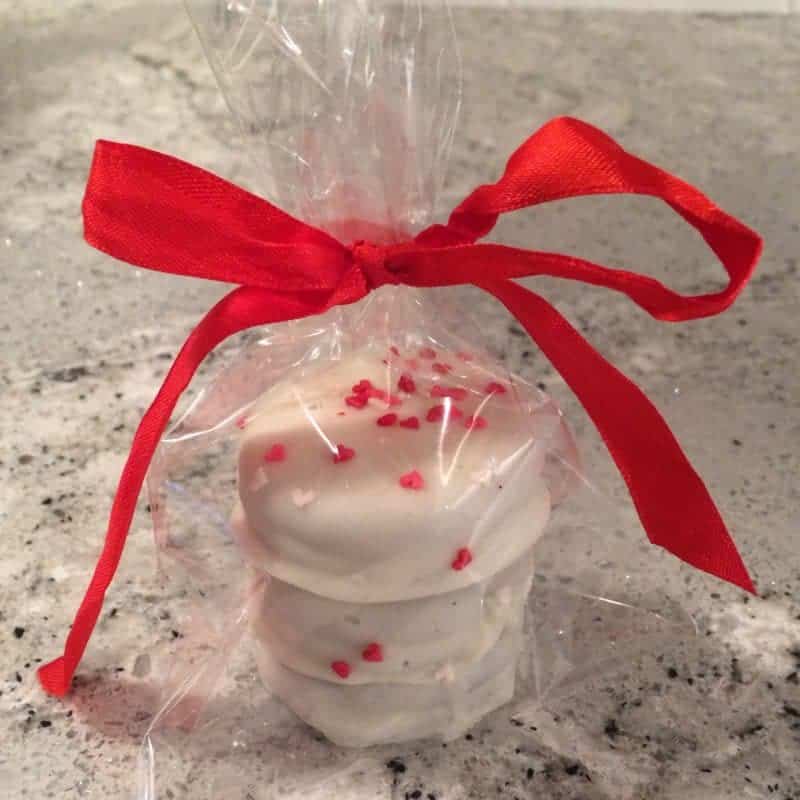 White chocolate covered Valentine's Day Oreo cookies with heart sprinkles in a cellophane baggie tied with red ribbon.