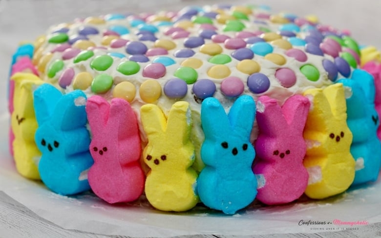 Vanilla frosted round Cake topped with pastel M&Ms and surrounded by marshmallow peeps.