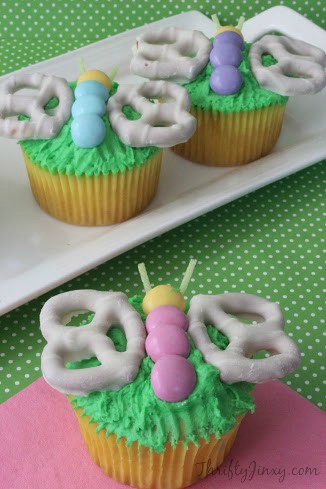 Vanilla cupcakes topped with green icing and butterflies made with M&Ms and white chocolate covered pretzels.