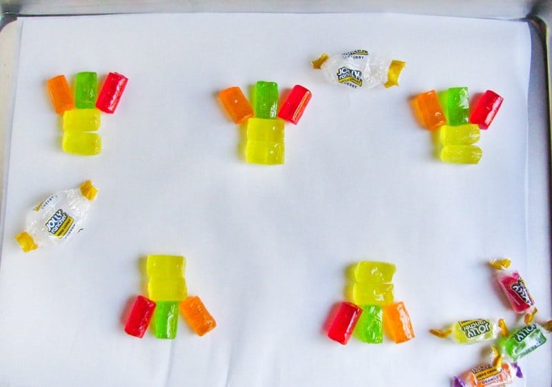 Unwrapped Jolly ranchers arranged on lined cookie sheet with two yellow candies on top of one another horizontally and red, orange, and green candies standing up vertically on top to look like feathers.