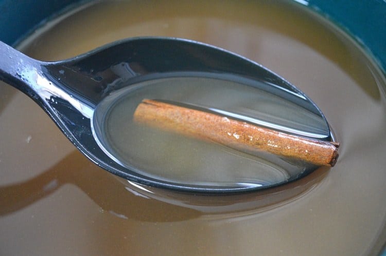 Spoon scooping up apple cider and cinnamon stick from slow cooker