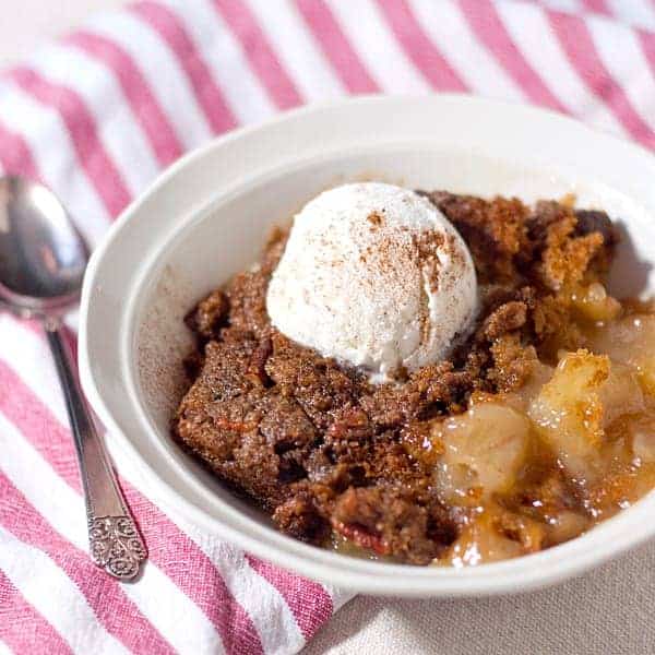 Bowl of cobbler with scoop of ice cream on top and a silver spoon next to it.