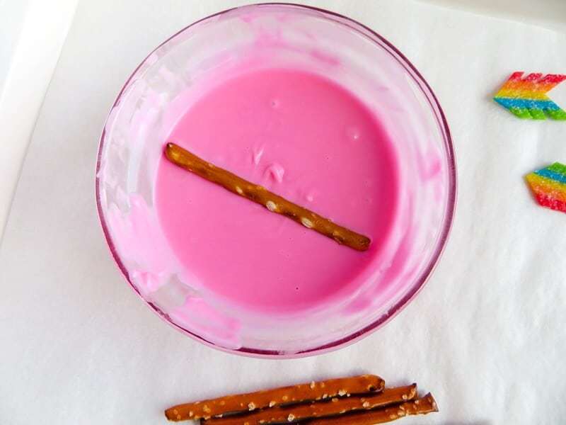 Pretzel sticks being dipped in melted pink candy.