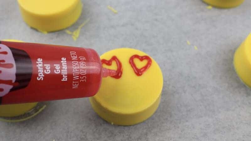 Heart eyes being drawn on yellow cookies with red sparkle gel.