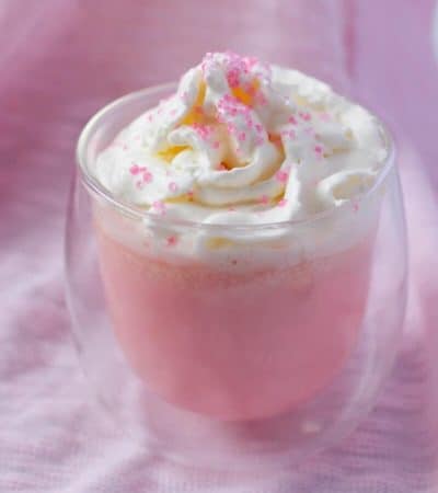 Pink hot chocolate in glass mug with whipped cream and pink sprinkles.