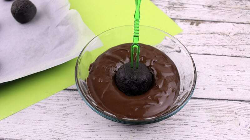 Oreo ball being dipped in melted chocolate using a toothpick.