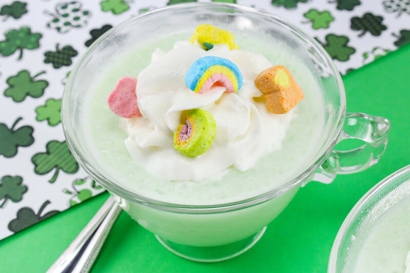 Green frozen drink in glass mug topped with whipped cream and lucky charms marshmallows.