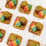 St. Patrick's Day pretzel bites made from square pretzels topped with rolo candies, gold sprinkles, and rainbow airheads.