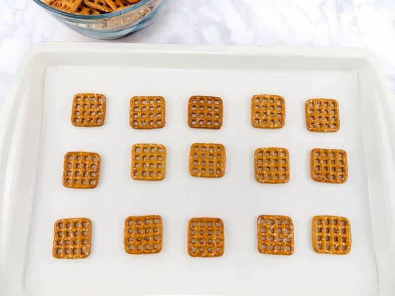 15 square pretzels arranged in 3 rows on a lined baking sheet.
