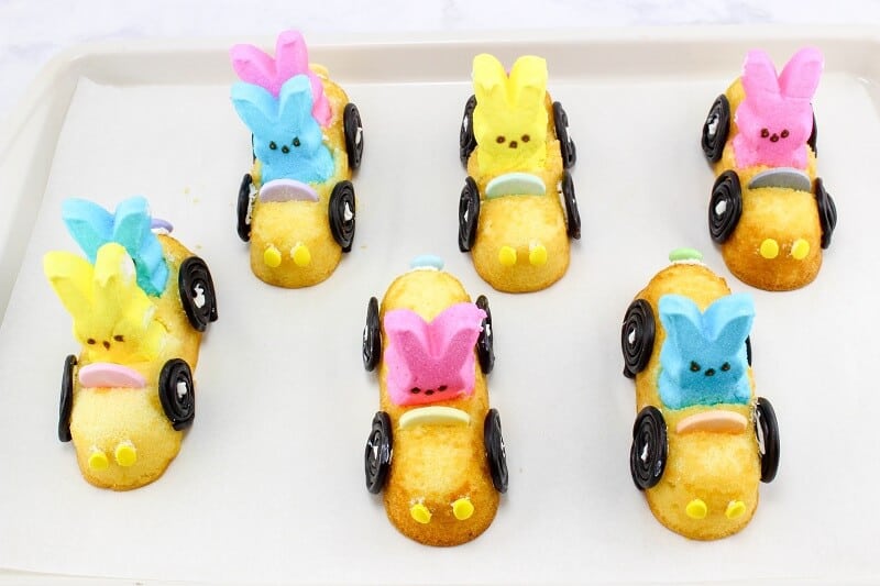 Six Peeps Twinkie cars on lined baking sheet setting after having their wheels stuck on with melted candy melts.