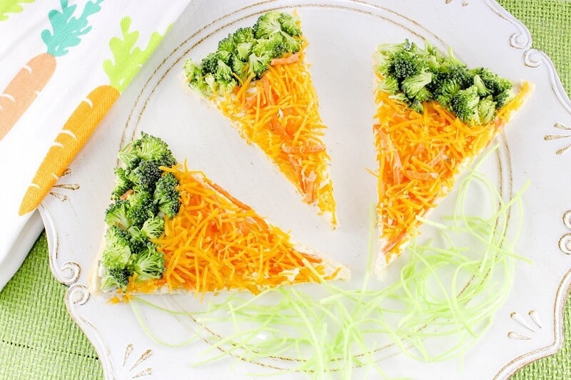 Triangular shaped slices of crescent roll pizza with shredded carrots and broccoli, arranged with brocolli "crust" and carrot sauce to resemble like carrots. 