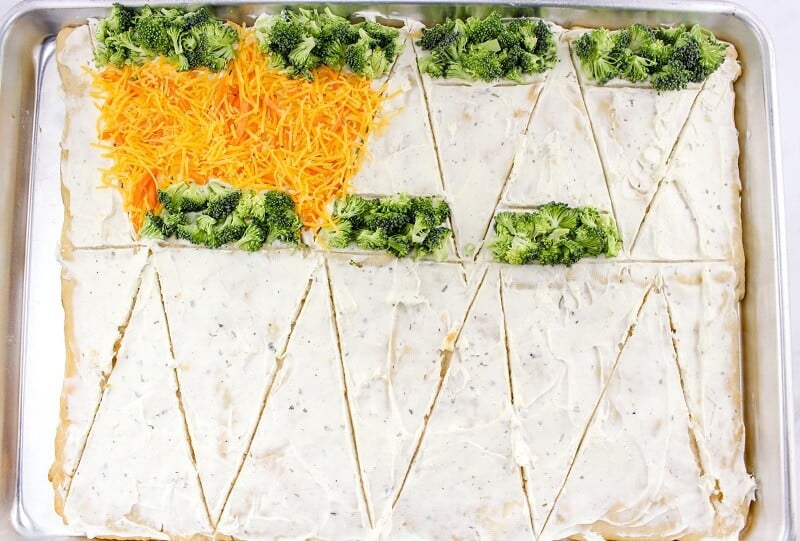 Crescent roll dough sliced into triangles and topped with broccoli florets  and shredded cheese and carrots.