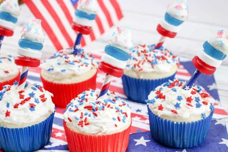 4th of July firecracker cupcakes surrounded by red, white, and blue party decor.