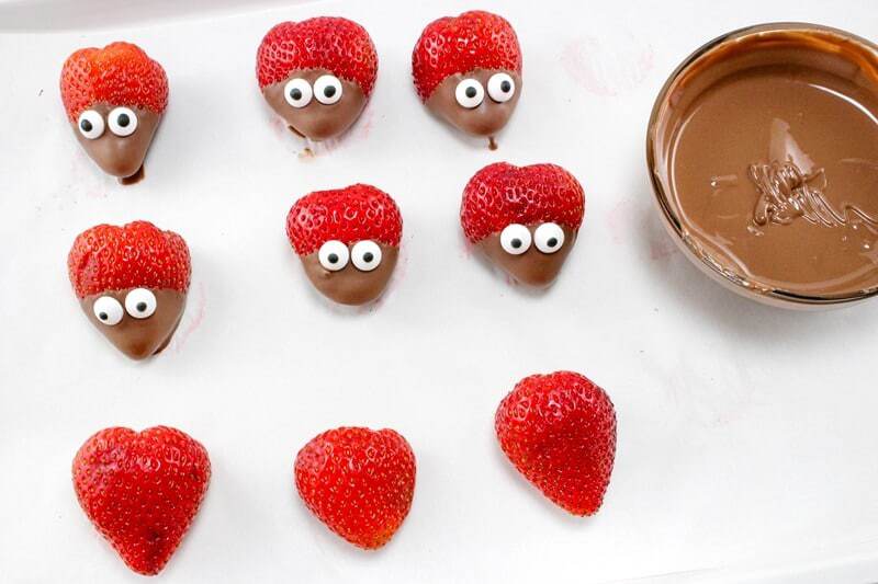 Strawberries with their bottom third dipped into melted chocolate and candy eyes pressed on top.