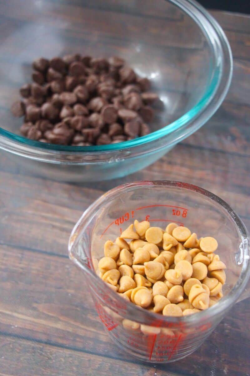 Glass bowl of chocolate chips and glass measuring cup with peanut butter chips.