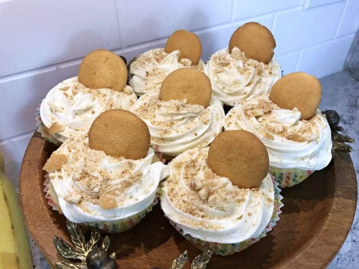 Banana pudding cupcakes topped with nilla wafers on wooden cake stand.