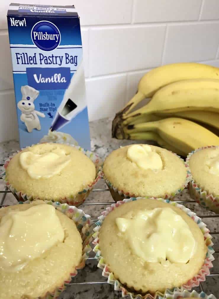 Banana pudding filled cupcakes with fresh bananas in the background.
