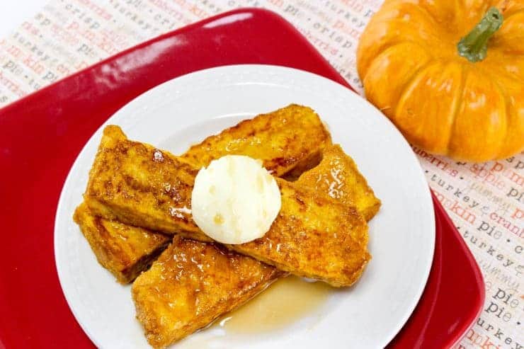 Three pumpkin French toast sticks on plate with syrup and butter.