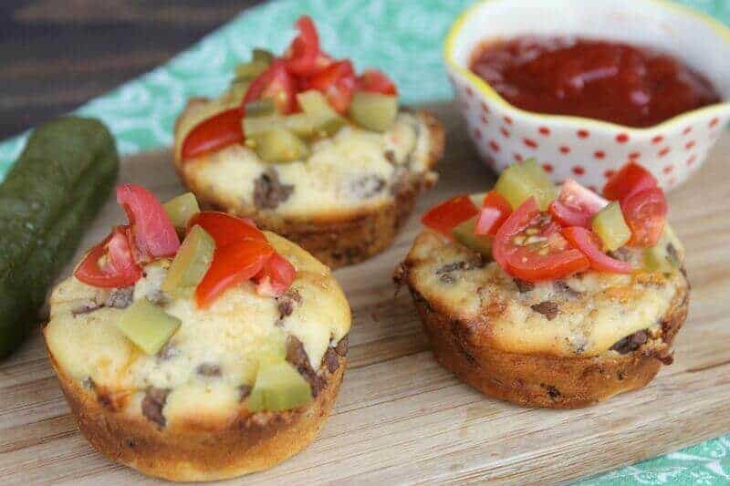 Cheeseburger muffins cups topped with chopped tomateos and pickles.