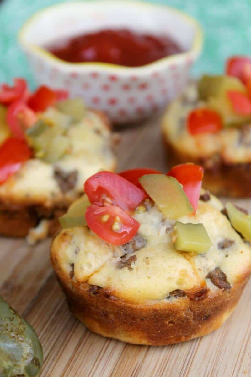 Loaded bacon cheeseburger muffin with tomato and pickles on top.