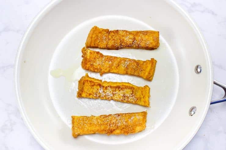 Four golden brown French toast sticks in frying pan, cooked to perfection.
