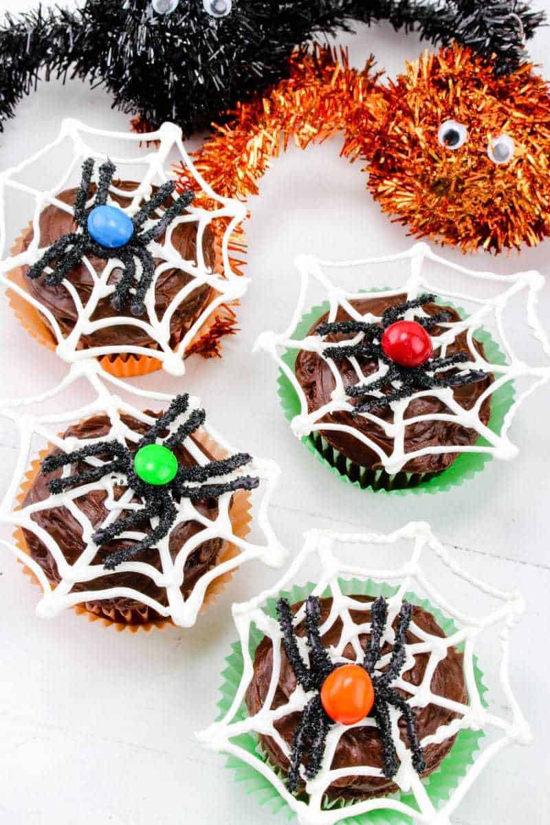 Four Halloween spider web cupcakes with blue, red, green, and orange M&Ms s the spider's bodies.