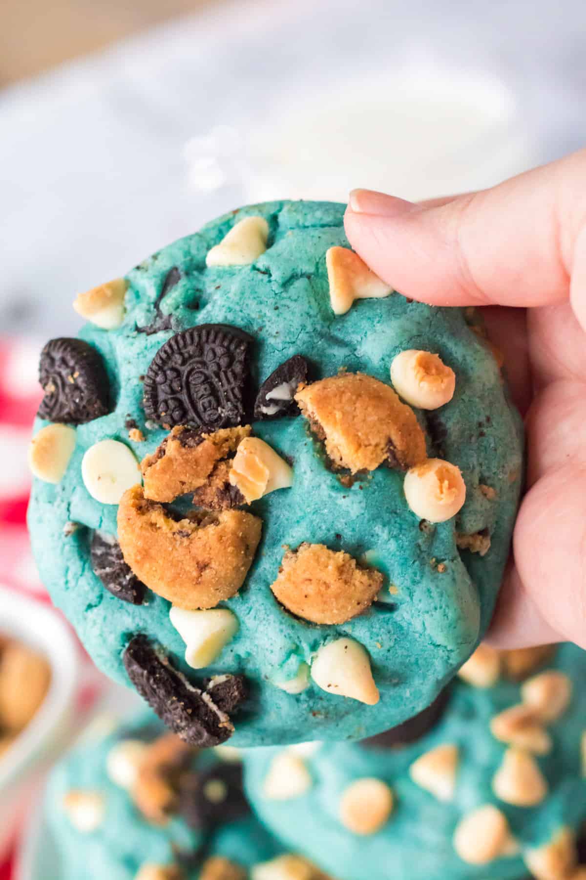 Hand holding large jumbo cookie monster cookies loaded with white chocolate chips and chunks of oreo and chocoalte chip cookies.