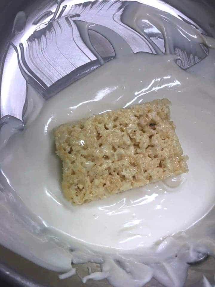 Rice krispie treat being dipped in white chocolate.