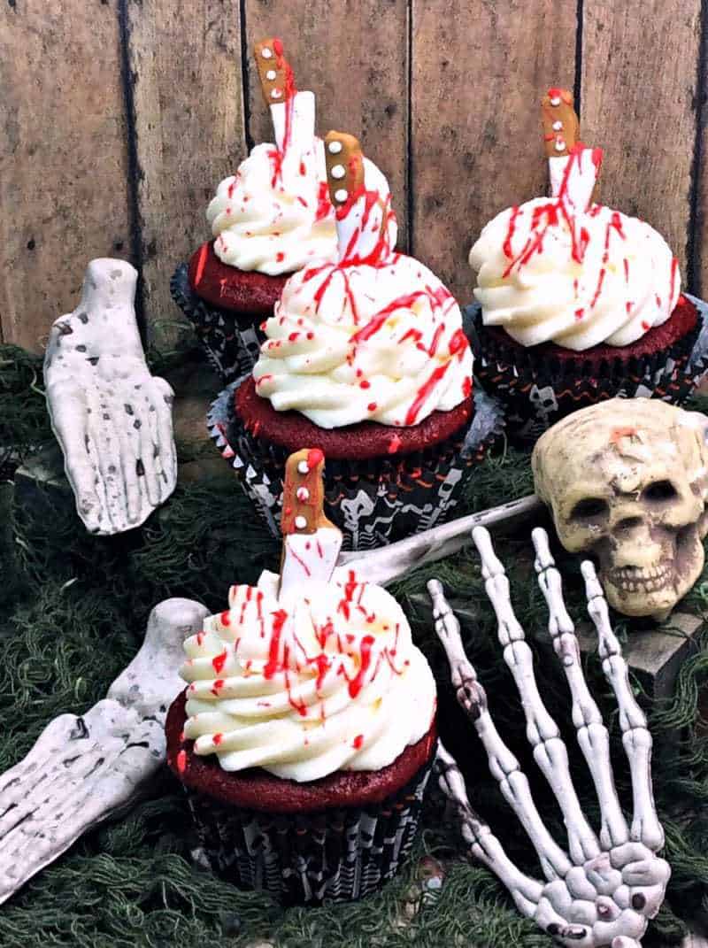 Bloody red velvet cupcakes surrounded by spooky Halloween decorations.