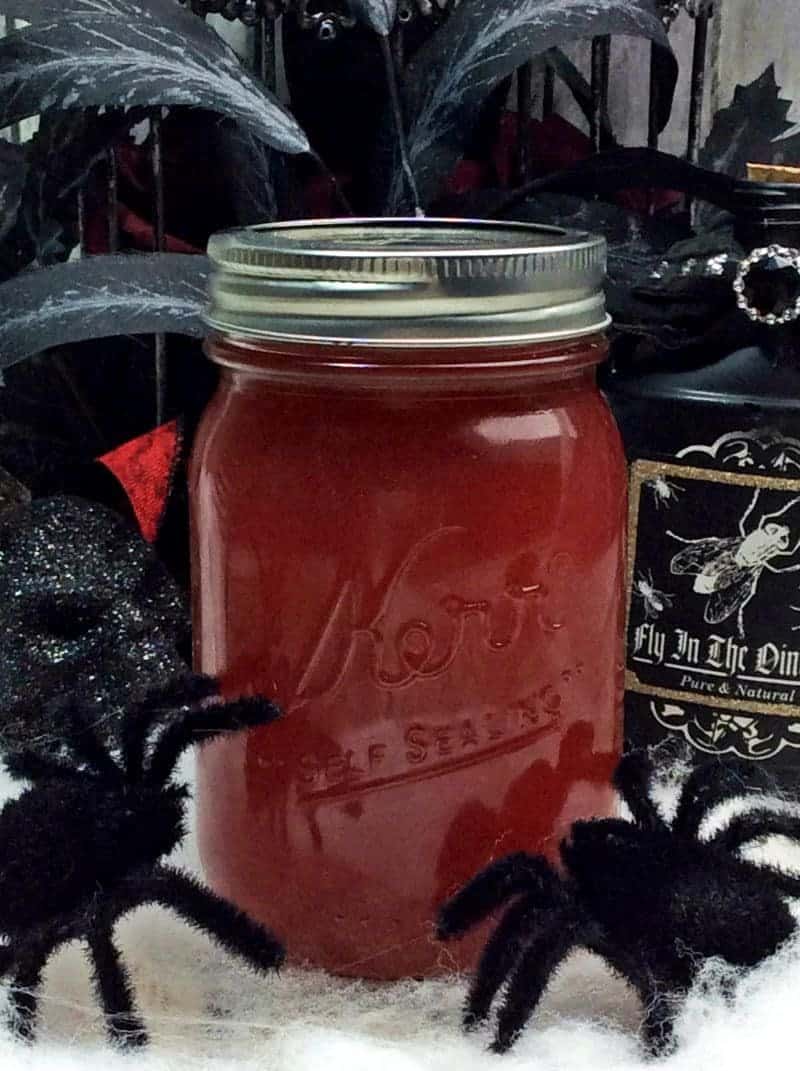 Black widow venom moonshine in a sealed mason jar surrounded by Halloween decorations.