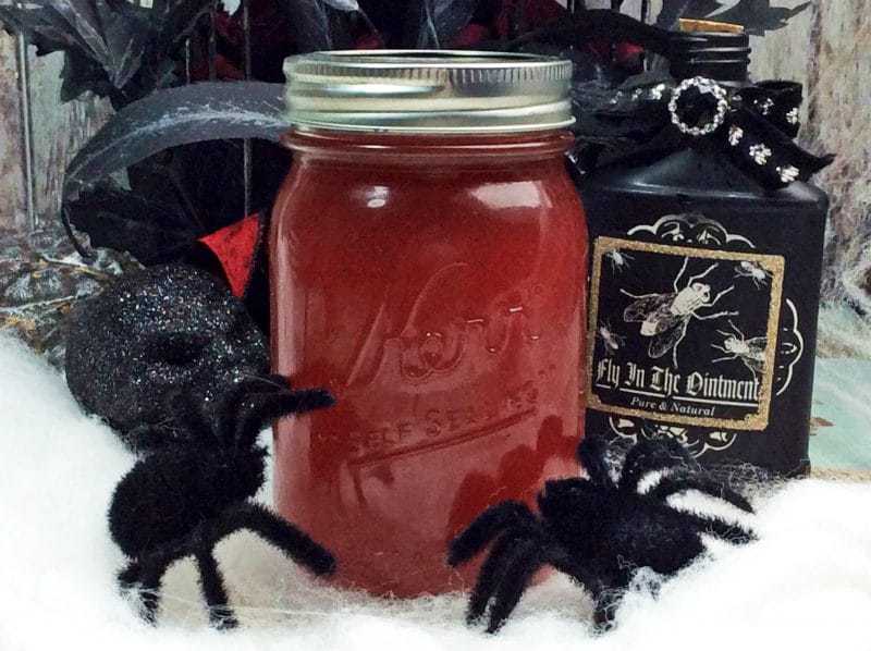 Dark red moonshine in mason jar surrounded by Halloween decorations such as black flowers, a skull, and fuzzy spiders. 