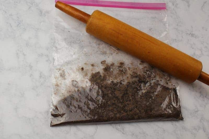 Chocolate cookies in baggie being crushed with rolling pin.