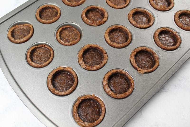 Baked brownie bites with round circle pressed into them while still in pan.