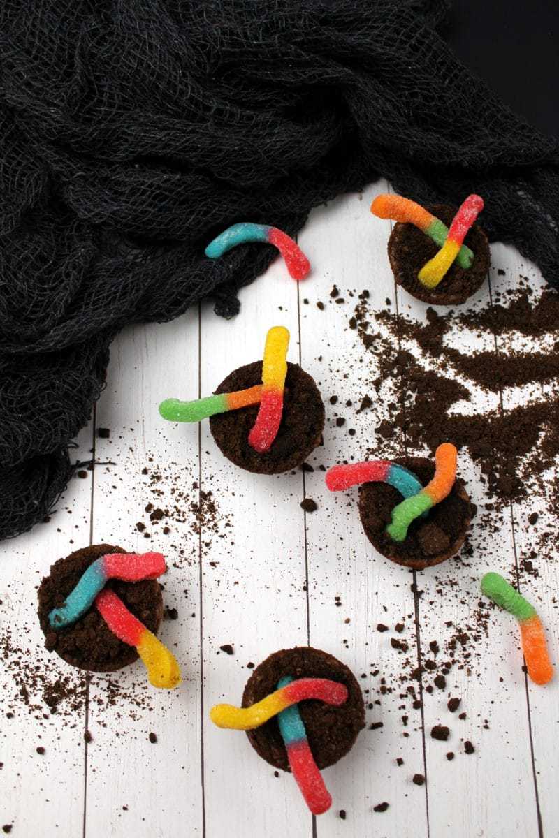 Overhead shot of dirt cup brownie bites with colorful gummy worms and cookie crumbs around them.