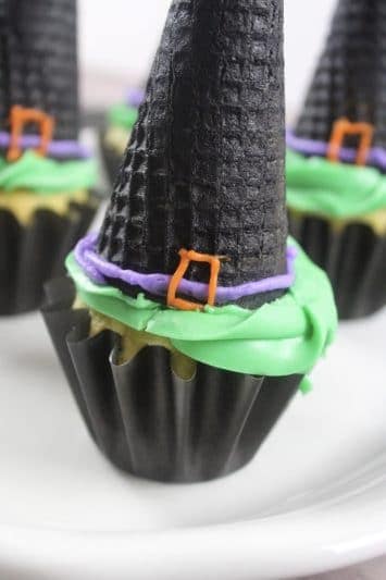 Witch hat cupcakes are made by topping cupcakes with sugar cones and adding detail with icing. These Halloween cupcakes will be a hit at a Halloween party.