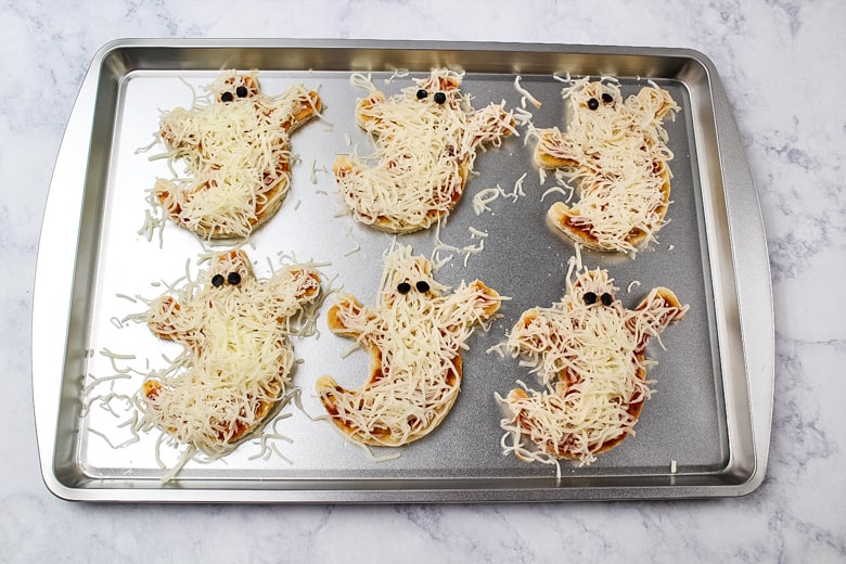 6 ghost pizza crusts covered in pizza sauce, shredded cheese, and with small pieces of black olives as eyes