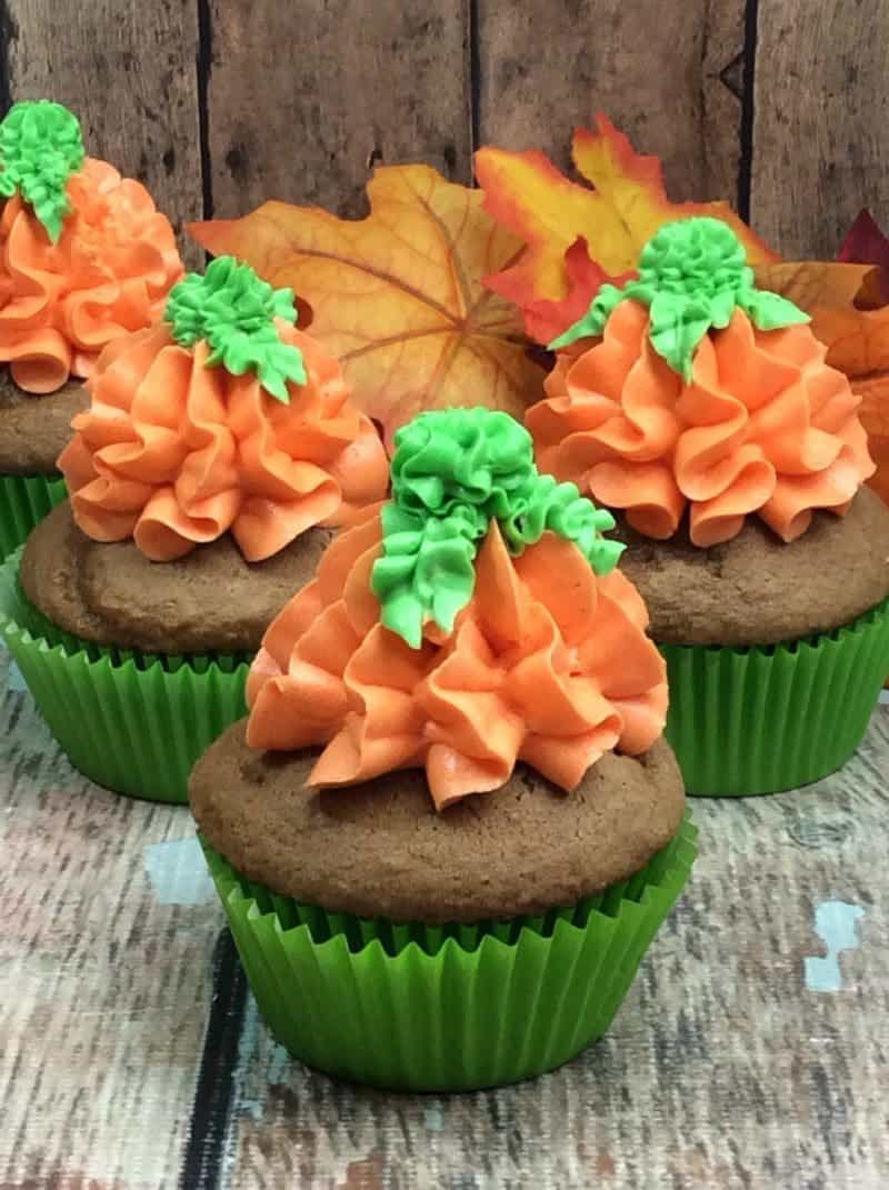 Pumpkin spice cupcakes topped with orange and green frosting in the shape of a pumpking.