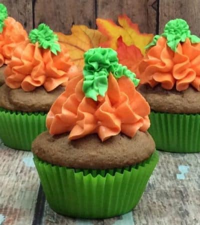 Pumpkin spice cupcakes with orange and green frosting piped on in the shape of a pumpkin.