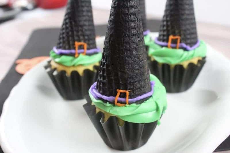 Witch hat cupcakes are made by topping cupcakes with sugar cones and adding detail with icing. These Halloween cupcakes will be a hit at a Halloween party.