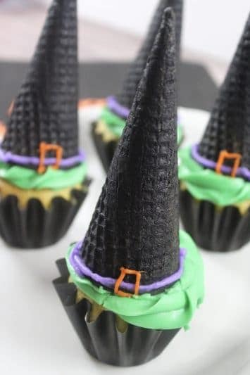 Witch hat cupcakes are made by topping cupcakes with sugar cones and adding detail with icing. These Halloween cupcakes will be a hit at a Halloween party.