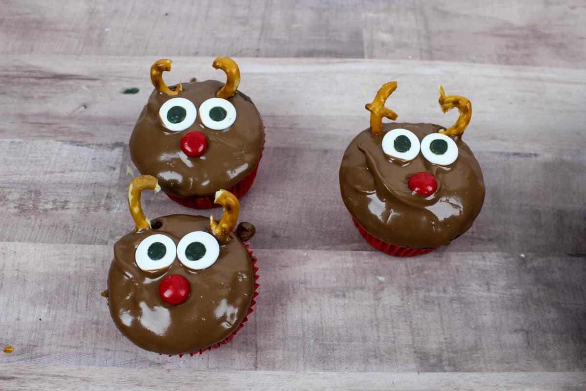 Three adorable reindeer cupcakes with candy eyes, red M&M noes, and pretzel antlers.