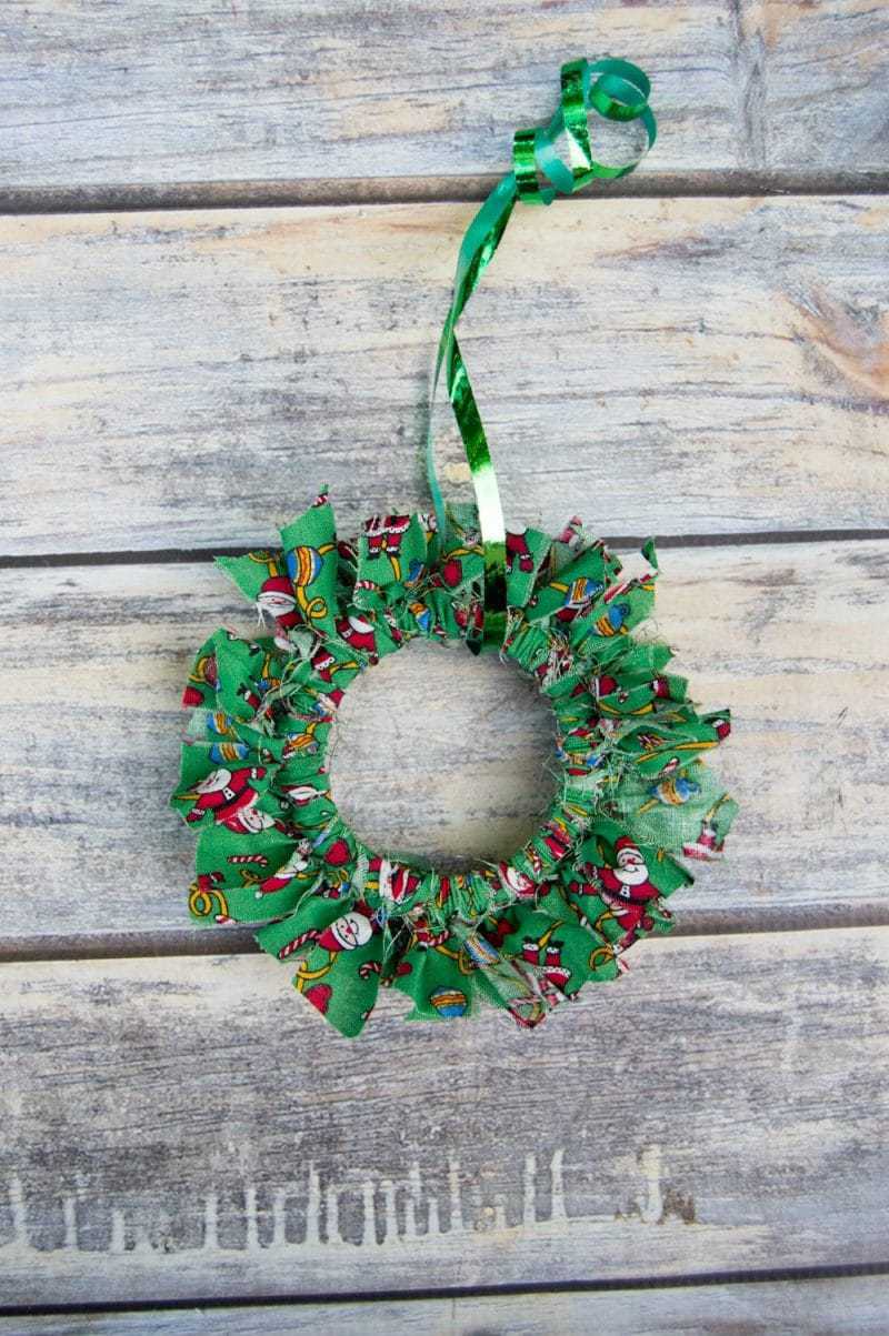 Mason canning jar lid Christmas wreath ornament made with strips of christmas fabric.