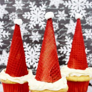 Santa hat cupcakes are made by topping cupcakes with red sugar cones and a mini marshmallow. These fun and easy Christmas cupcakes will definitely be a hit!