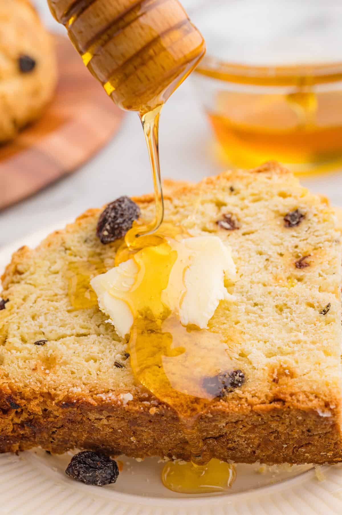 Slice of Irish soda bread with raisins and caraway seeds topped with butter and honey drizzle