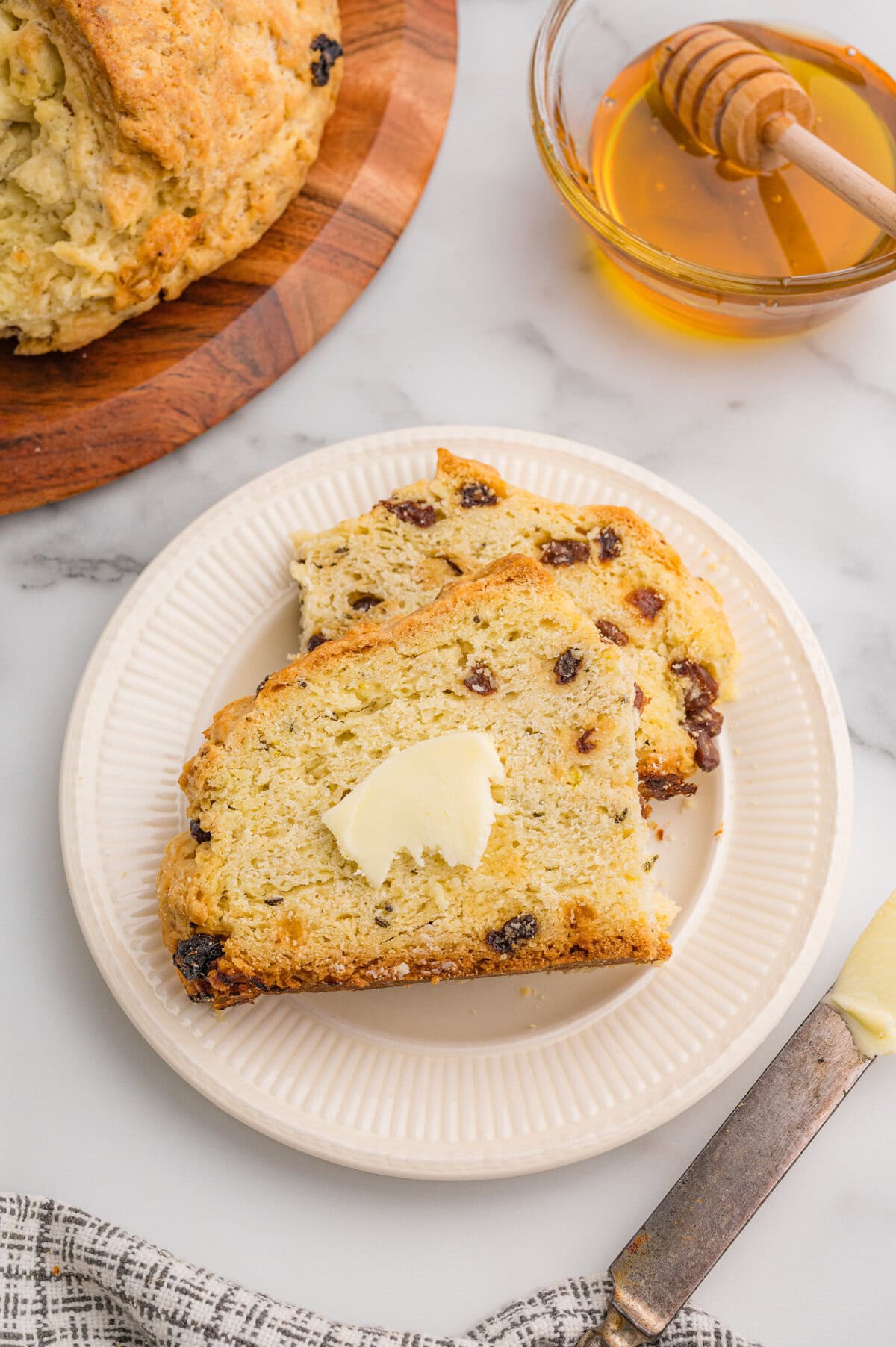 Two slices of Irish soda bread with raisins and caraway seeds on a white plate with butter