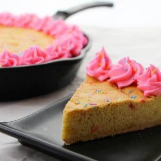 A cast iron skillet cookie recipe for a gigantic sugar cookie with rainbow sprinkles and homemade pink frosting. The sprinkles give the skillet cookie a funfetti vibe, making it perfect for birthday parties or other celebrations.