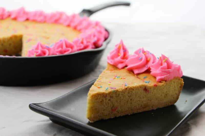 A cast iron skillet cookie recipe for a gigantic sugar cookie with rainbow sprinkles and homemade pink frosting. The sprinkles give the skillet cookie a funfetti vibe, making it perfect for birthday parties or other celebrations.