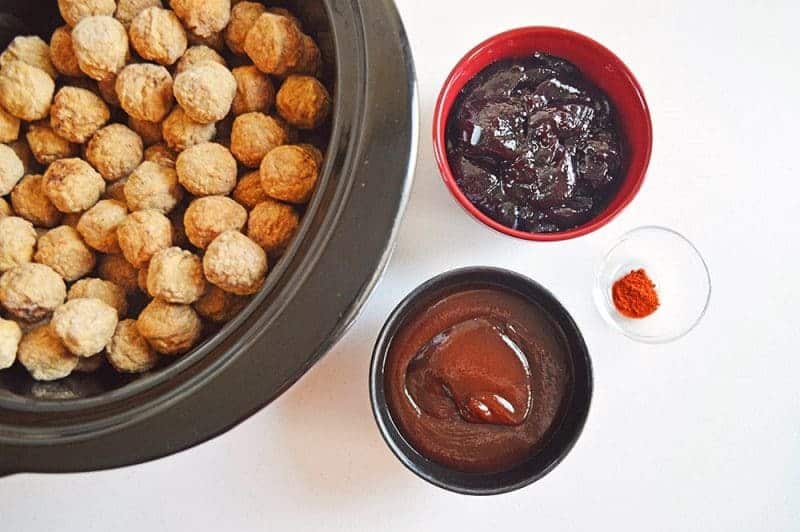 Frozen meatballs in crock pot and bowls of grape jelly, BBQ sauce, and cayenne pepper.